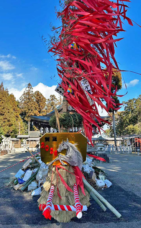 今年の干支を額に飾られた左義長の山車、後ろには正月飾り